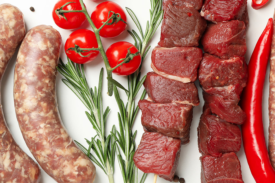 Frisches Grillfleisch und Würste mit Kräutern, Tomaten und Chili.